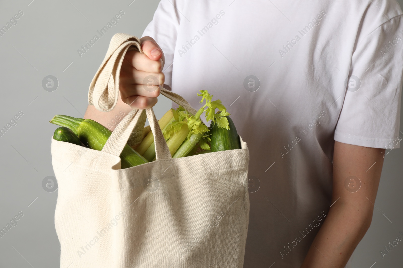 Photo of Woman holding shopper bag with groceries on light grey background, closeup. Eco friendly lifestyle