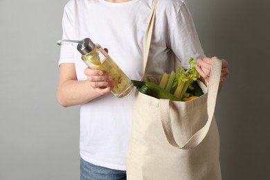 Photo of Woman holding shopper bag with groceries on light grey background, closeup. Eco friendly lifestyle