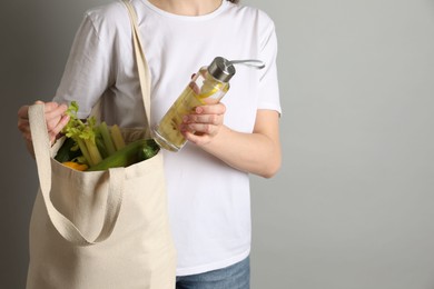 Photo of Woman holding shopper bag with groceries on light grey background, closeup and space for text. Eco friendly lifestyle