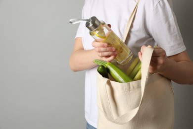 Photo of Woman holding shopper bag with groceries on light grey background, closeup and space for text. Eco friendly lifestyle