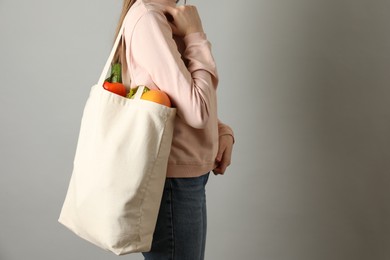 Photo of Woman holding shopper bag with groceries on light grey background, closeup. Eco friendly lifestyle