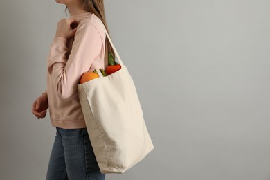 Photo of Woman holding shopper bag with groceries on light grey background, closeup and space for text. Eco friendly lifestyle