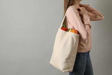 Photo of Woman holding shopper bag with groceries on light grey background, closeup and space for text. Eco friendly lifestyle