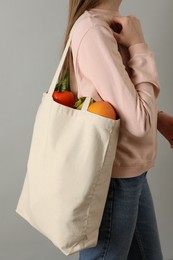 Photo of Woman holding shopper bag with groceries on light grey background, closeup. Eco friendly lifestyle