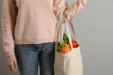 Photo of Woman holding shopper bag with groceries on light grey background, closeup. Eco friendly lifestyle