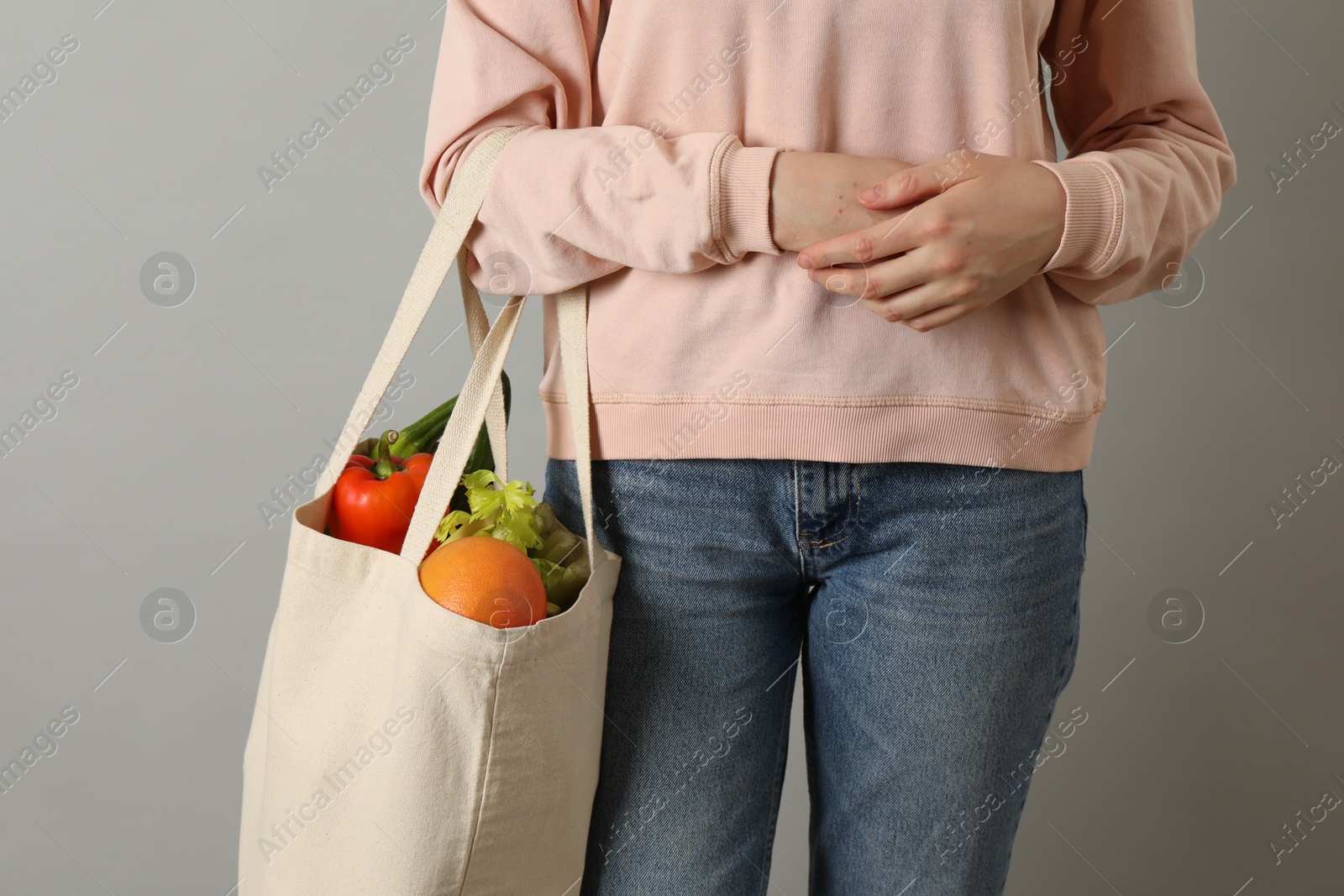 Photo of Woman holding shopper bag with groceries on light grey background, closeup. Eco friendly lifestyle