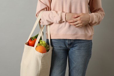 Photo of Woman holding shopper bag with groceries on light grey background, closeup. Eco friendly lifestyle