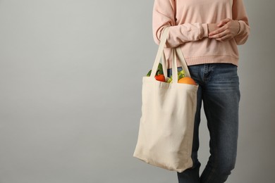 Photo of Woman holding shopper bag with groceries on light grey background, closeup and space for text. Eco friendly lifestyle