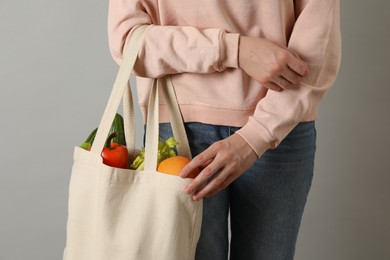 Photo of Woman holding shopper bag with groceries on light grey background, closeup. Eco friendly lifestyle