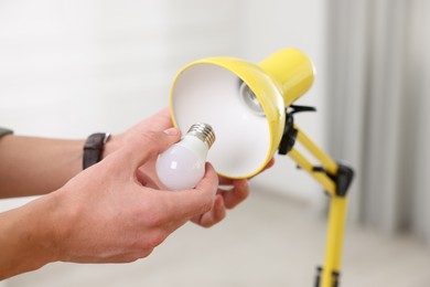 Photo of Man changing light bulb in lamp at home, closeup