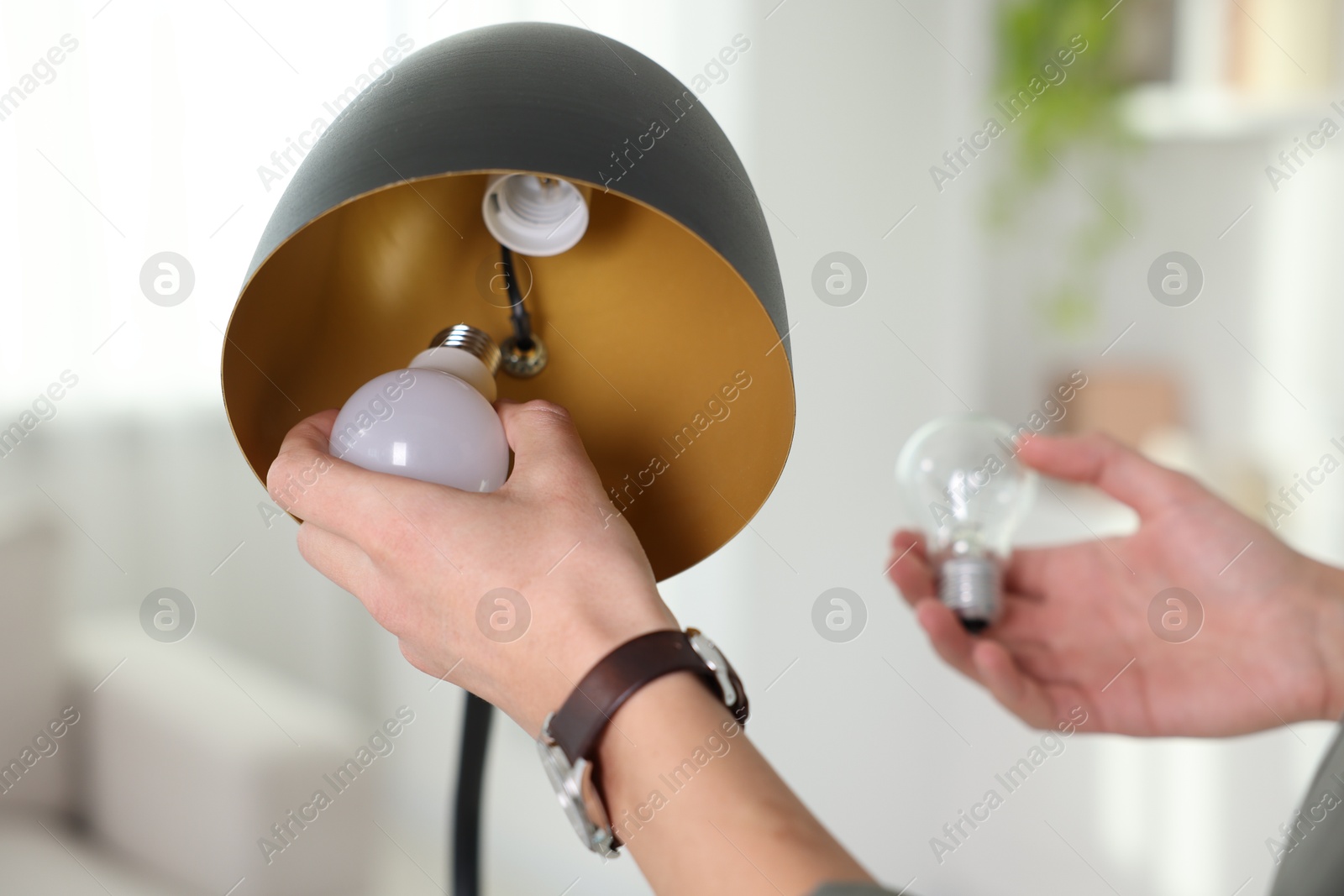 Photo of Man changing incandescent light bulb for fluorescent one in lamp at home, closeup