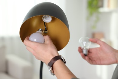 Photo of Man changing incandescent light bulb for fluorescent one in lamp at home, closeup