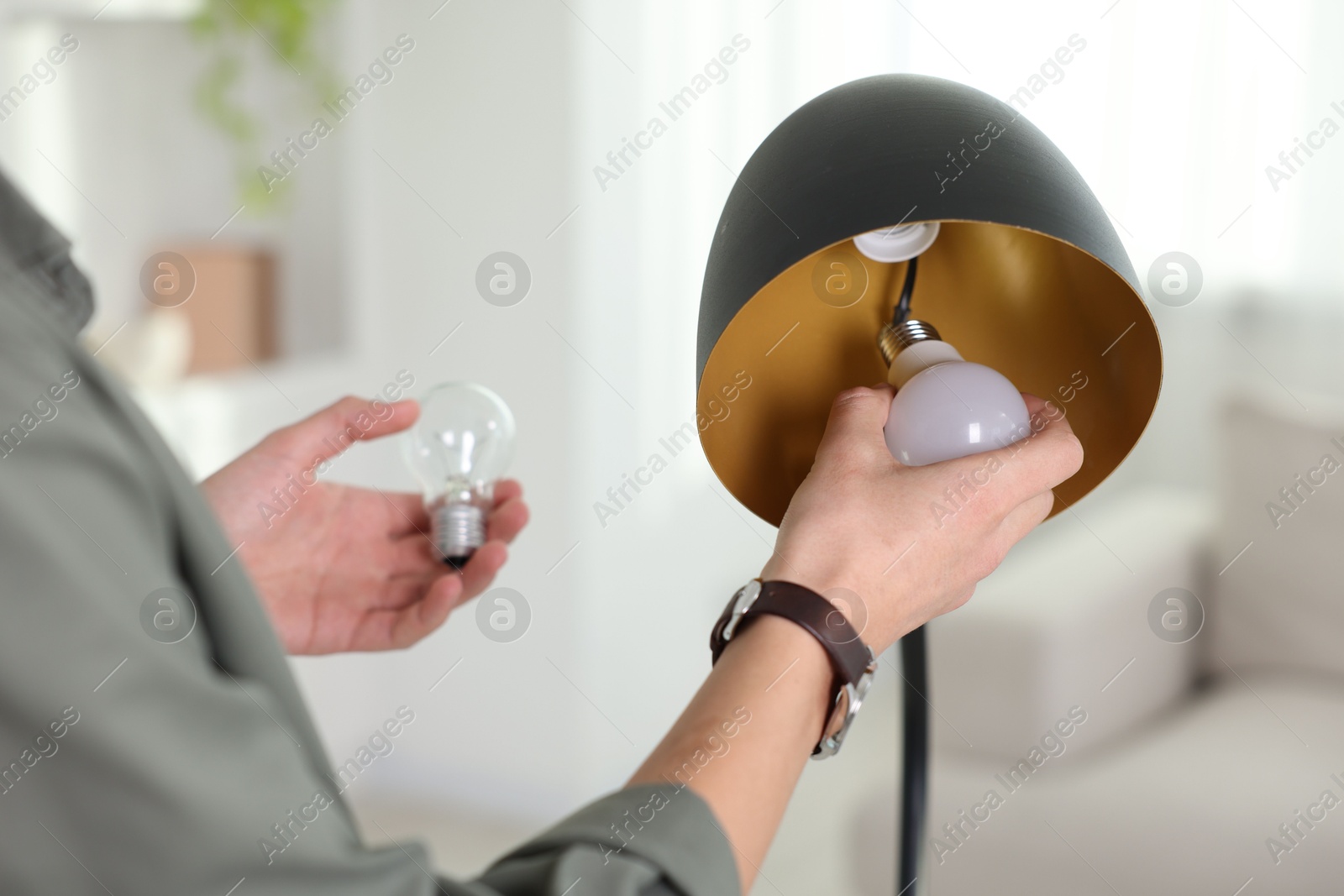 Photo of Man changing incandescent light bulb for fluorescent one in lamp at home, closeup