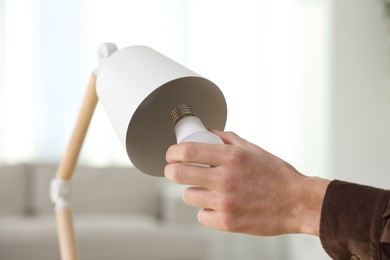 Photo of Man changing light bulb in lamp at home, closeup