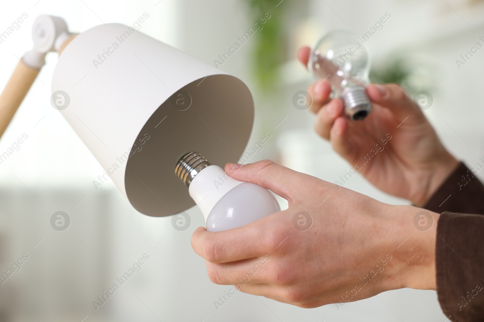 Photo of Man changing incandescent light bulb for fluorescent one in lamp at home, closeup