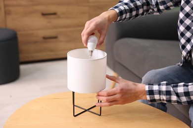 Photo of Man changing light bulb in lamp at home, closeup