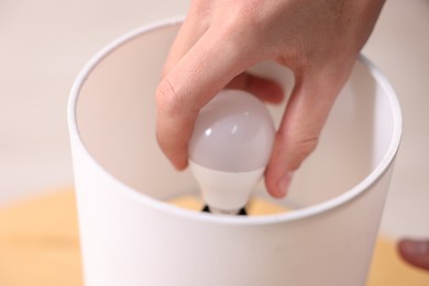 Photo of Man changing light bulb in lamp at home, closeup