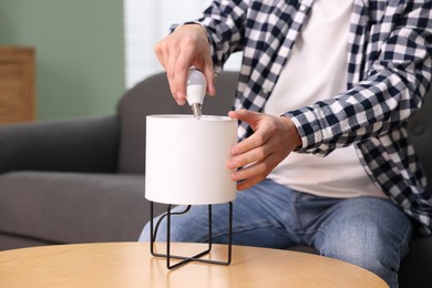 Photo of Man changing light bulb in lamp at home, closeup