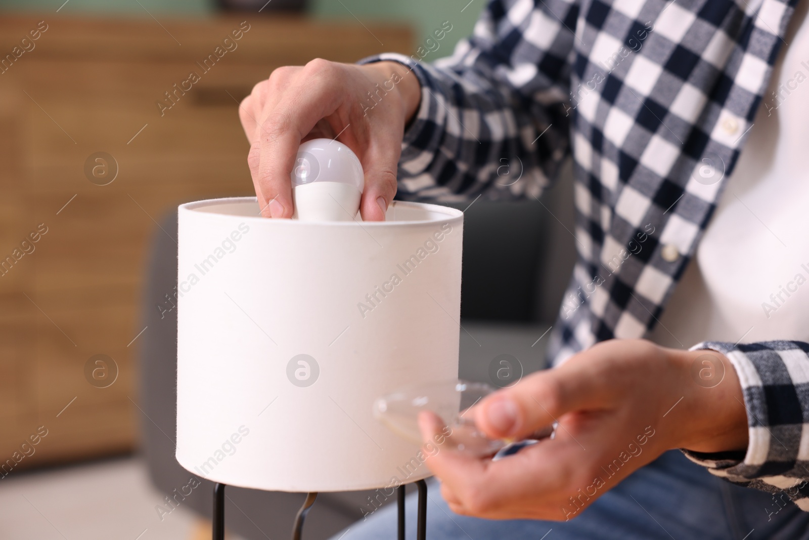 Photo of Man changing incandescent light bulb for fluorescent one in lamp at home, closeup