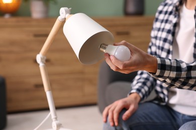 Photo of Man changing light bulb in lamp at home, closeup