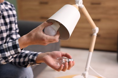 Photo of Man changing incandescent light bulb for fluorescent one in lamp at home, closeup