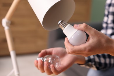 Photo of Man changing incandescent light bulb for fluorescent one in lamp at home, closeup