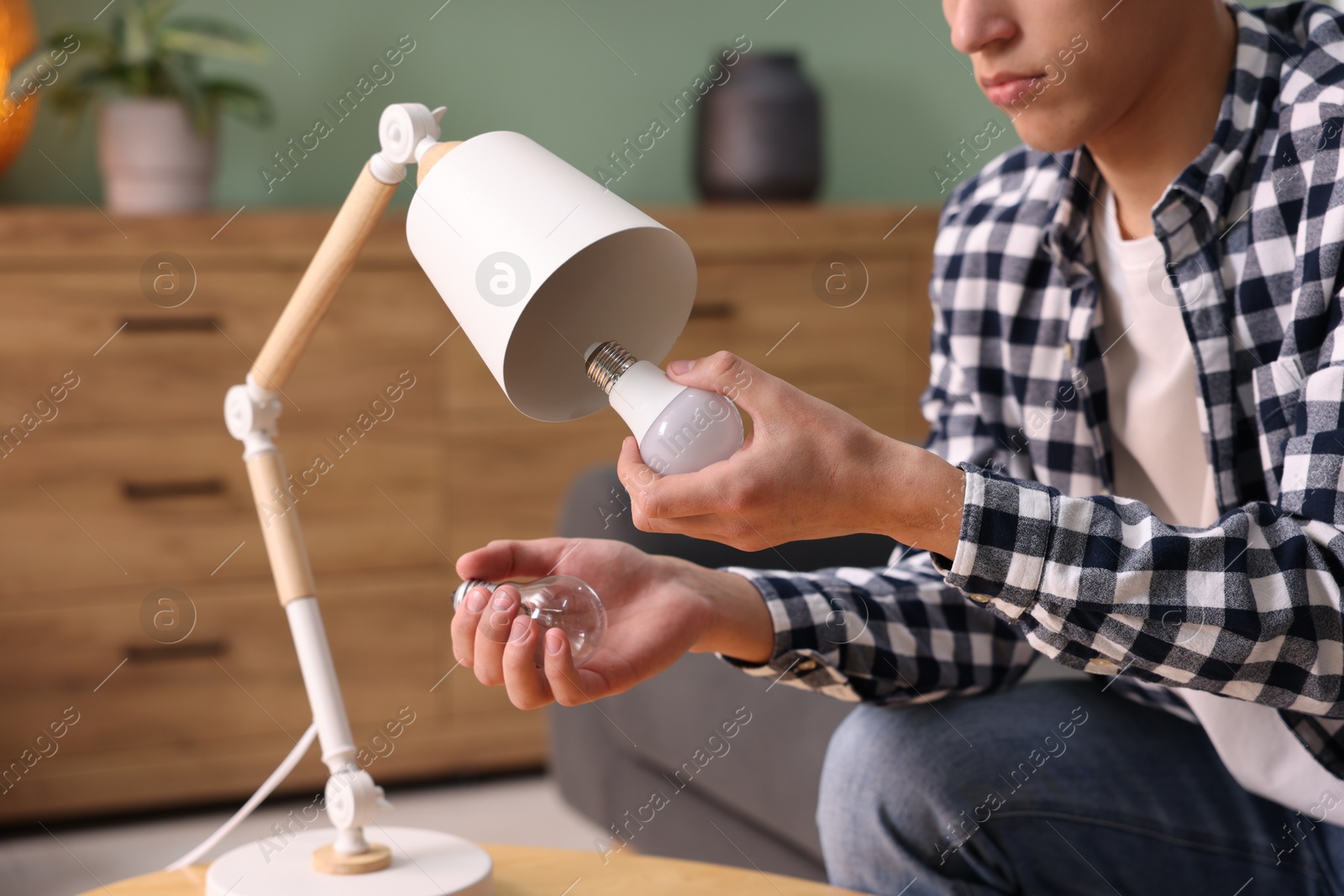 Photo of Man changing incandescent light bulb for fluorescent one in lamp at home, closeup