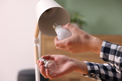 Photo of Man changing incandescent light bulb for fluorescent one in lamp at home, closeup