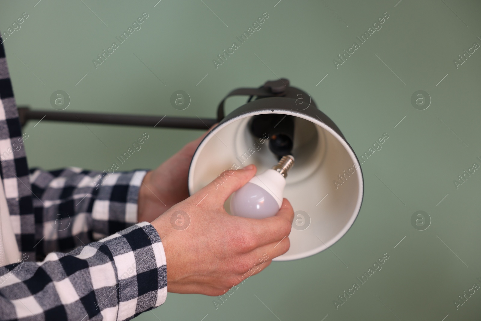 Photo of Man changing light bulb in lamp on greyish green background, closeup