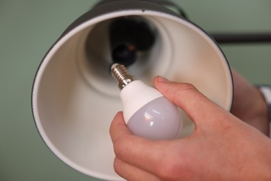 Photo of Man changing light bulb in lamp on greyish green background, closeup