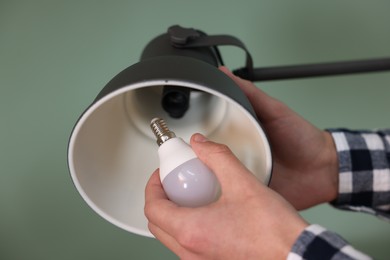 Photo of Man changing light bulb in lamp on greyish green background, closeup