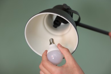 Photo of Man changing light bulb in lamp on greyish green background, closeup