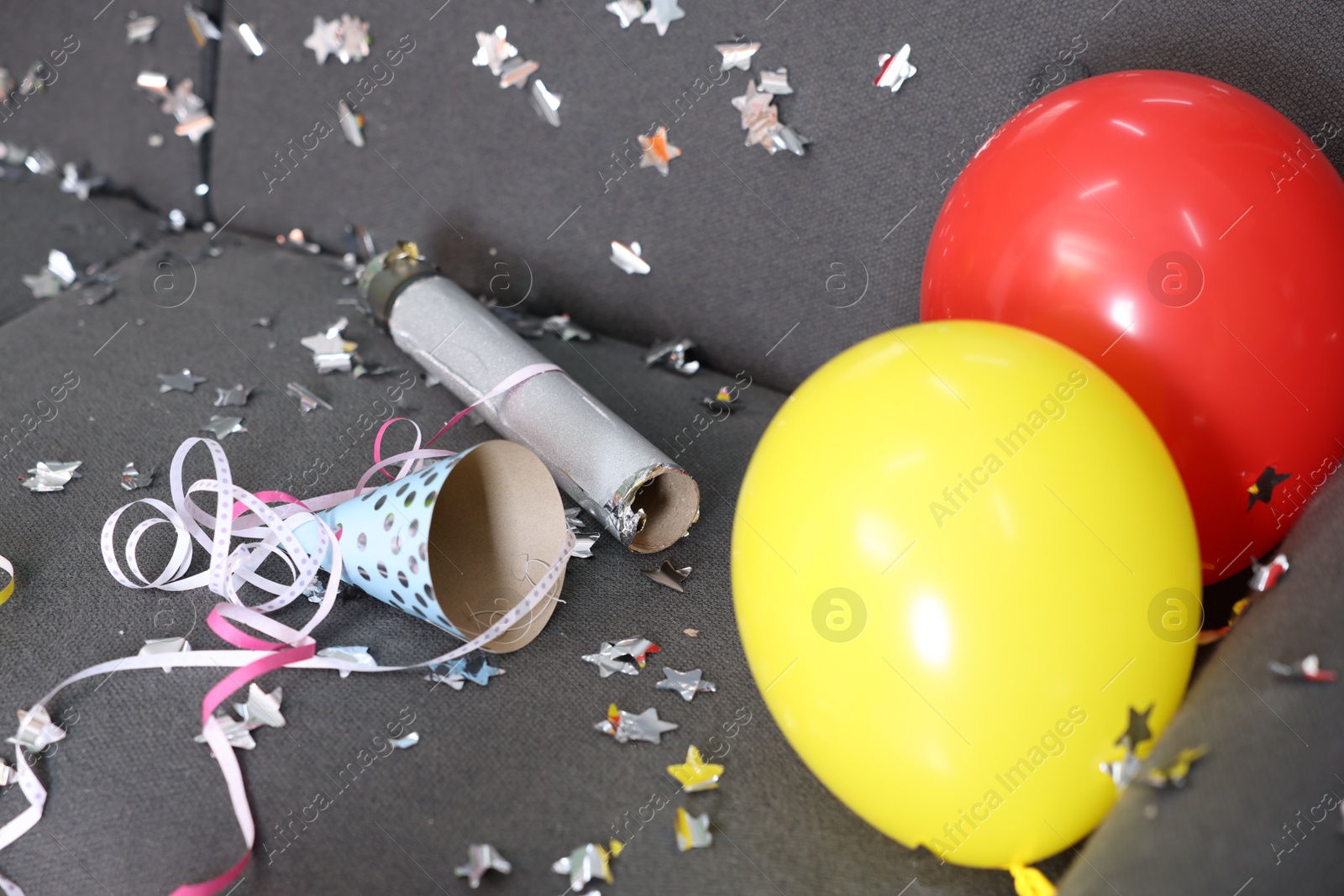 Photo of Shiny confetti, balloons and other party decor on sofa indoors