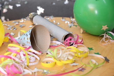 Photo of Confetti popper, serpentine streamers and other party decor on wooden table indoors, closeup