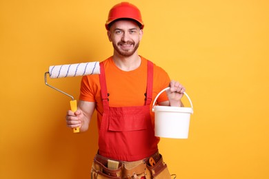 Photo of Professional painter with roller and bucket of paint on orange background