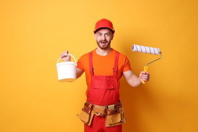 Photo of Emotional painter with roller and bucket of paint on orange background