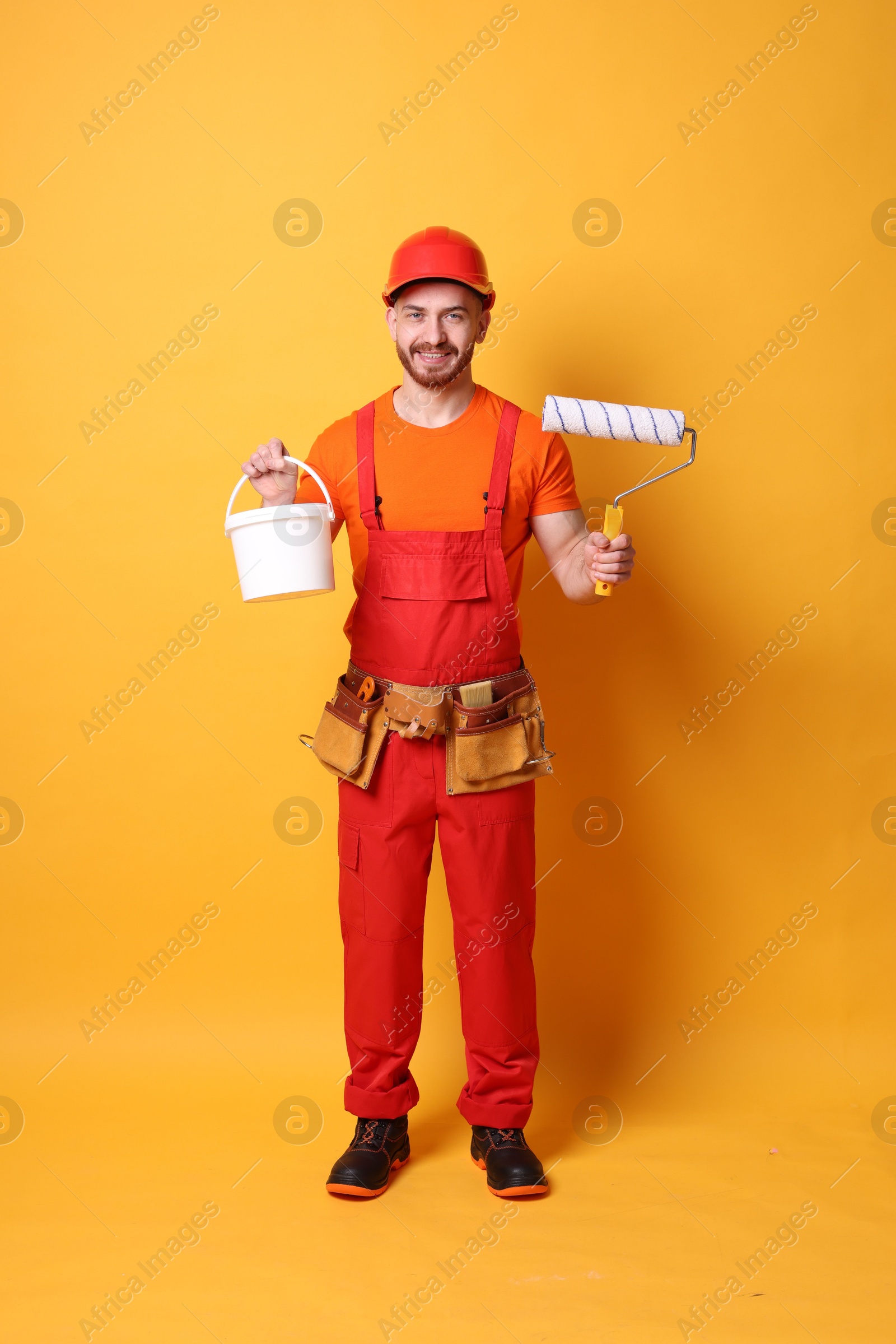 Photo of Professional painter with roller and bucket of paint on orange background