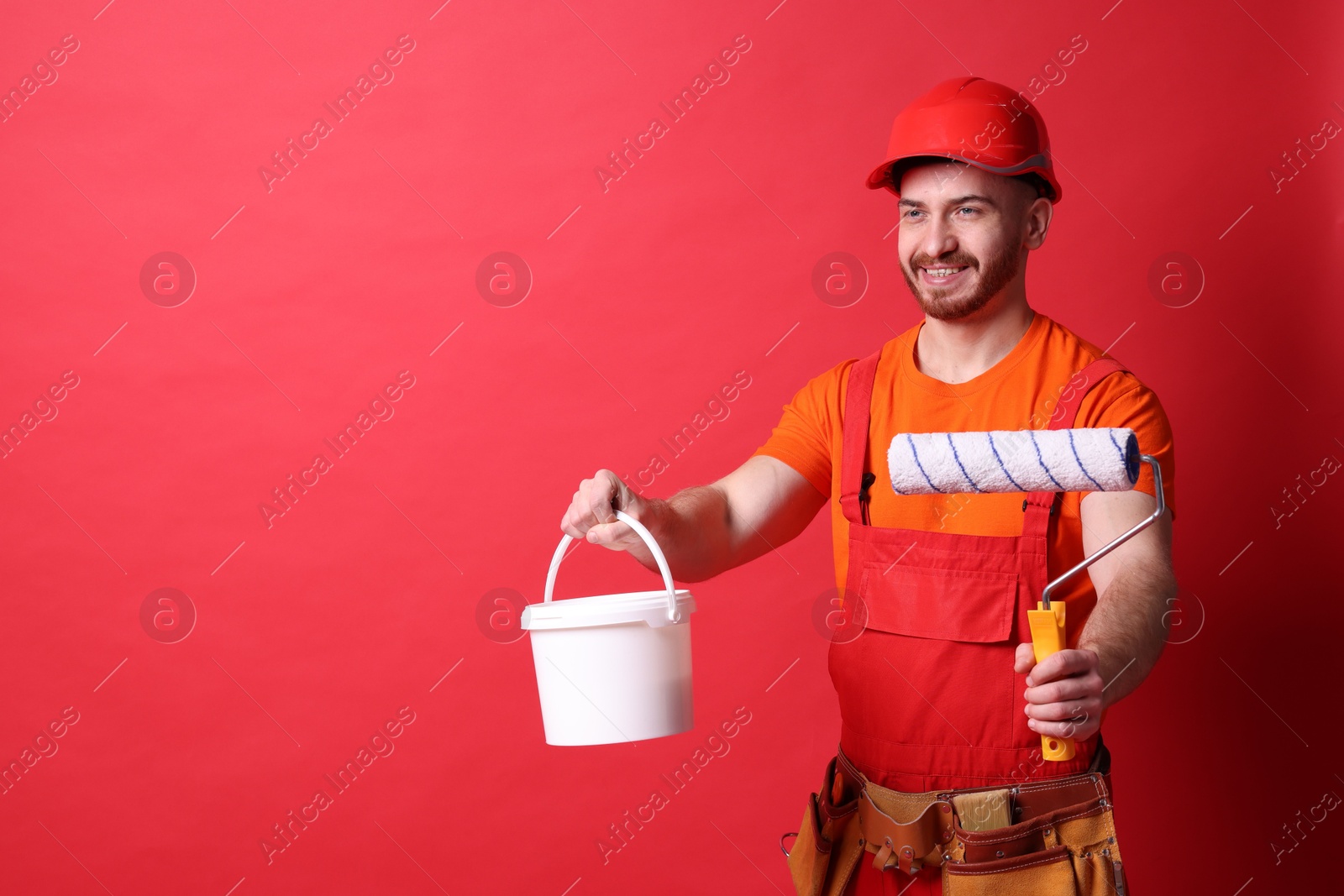 Photo of Professional painter with roller and bucket of paint on red background. Space for text