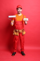 Photo of Professional painter with roller and brush on red background