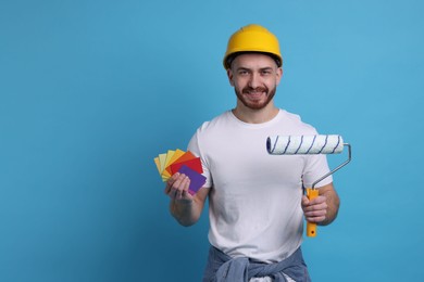 Photo of Man wearing hardhat with roller and color samples on blue background. Space for text