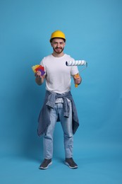 Photo of Man wearing hardhat with roller and color samples on blue background