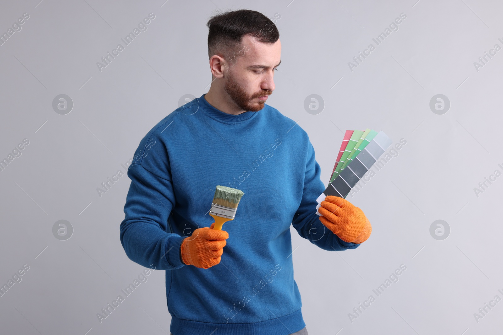 Photo of Man with paintbrush and color selection chart on light grey background