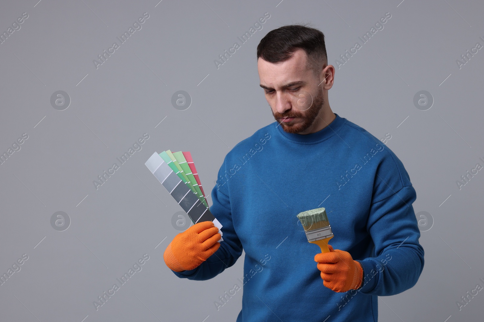 Photo of Man with paintbrush and color selection chart on light grey background