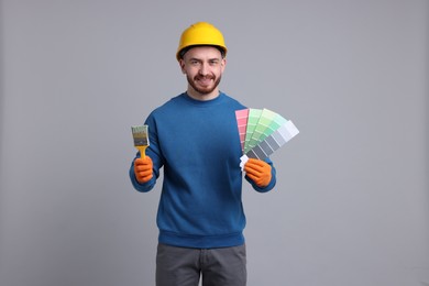 Photo of Man wearing hardhat with paintbrush and color selection chart on light grey background