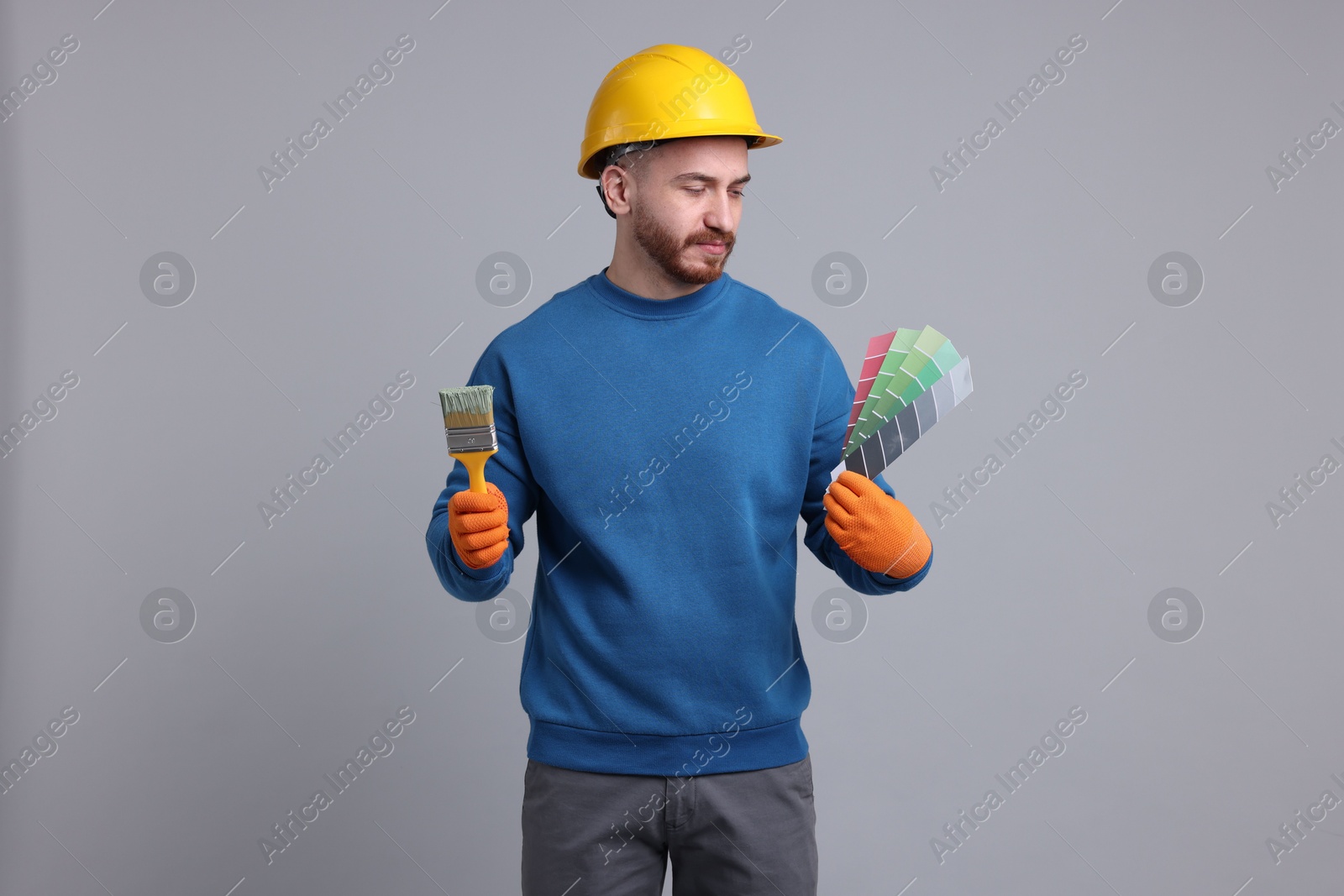 Photo of Man wearing hardhat with paintbrush and color selection chart on light grey background