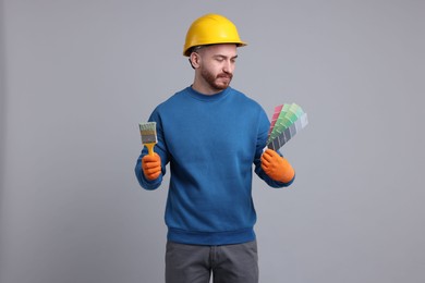 Photo of Man wearing hardhat with paintbrush and color selection chart on light grey background