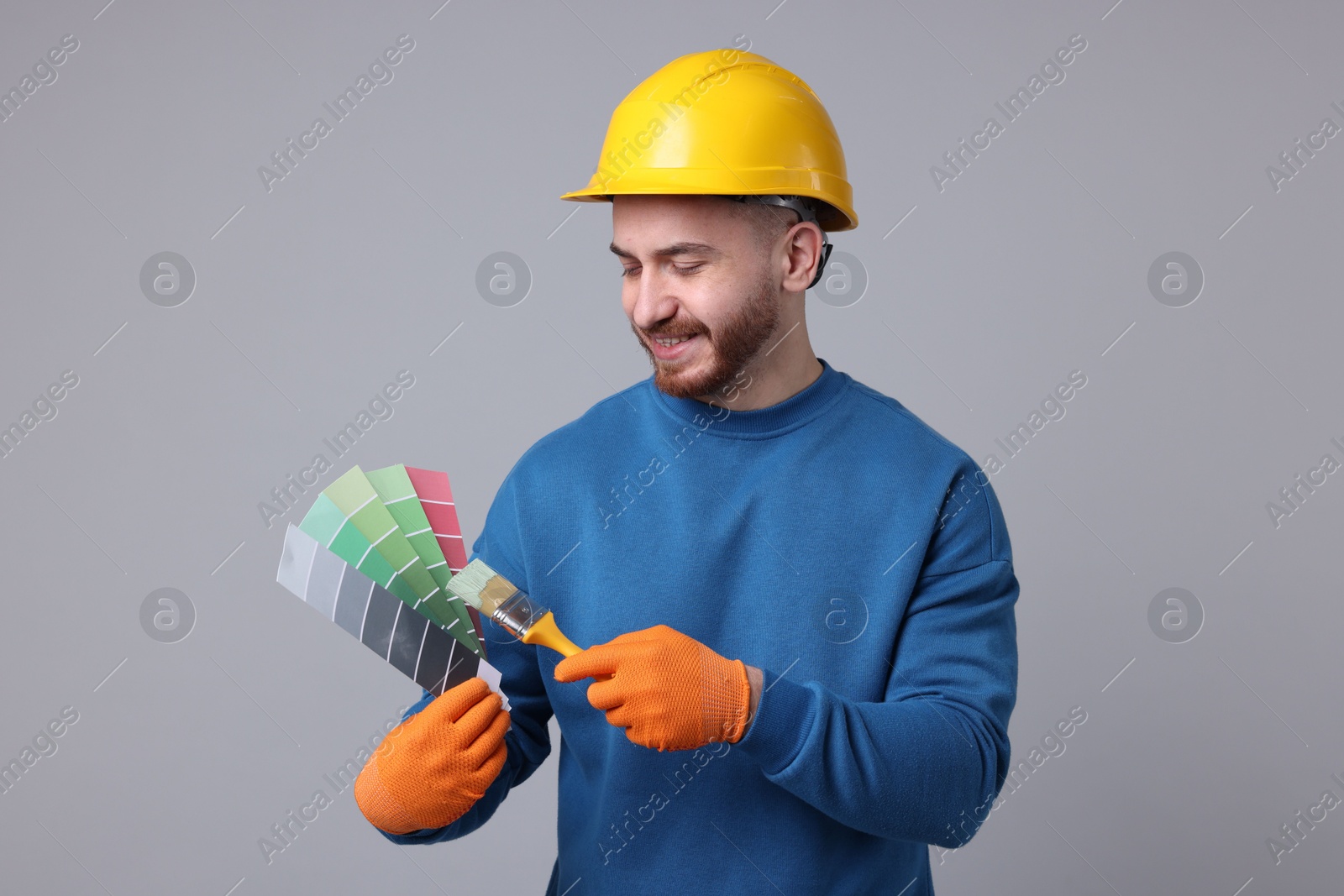 Photo of Man wearing hardhat with paintbrush and color selection chart on light grey background