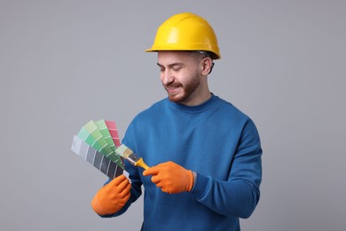 Photo of Man wearing hardhat with paintbrush and color selection chart on light grey background