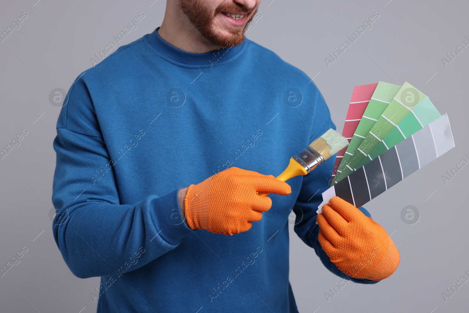 Photo of Man with paintbrush and color selection chart on light grey background, closeup