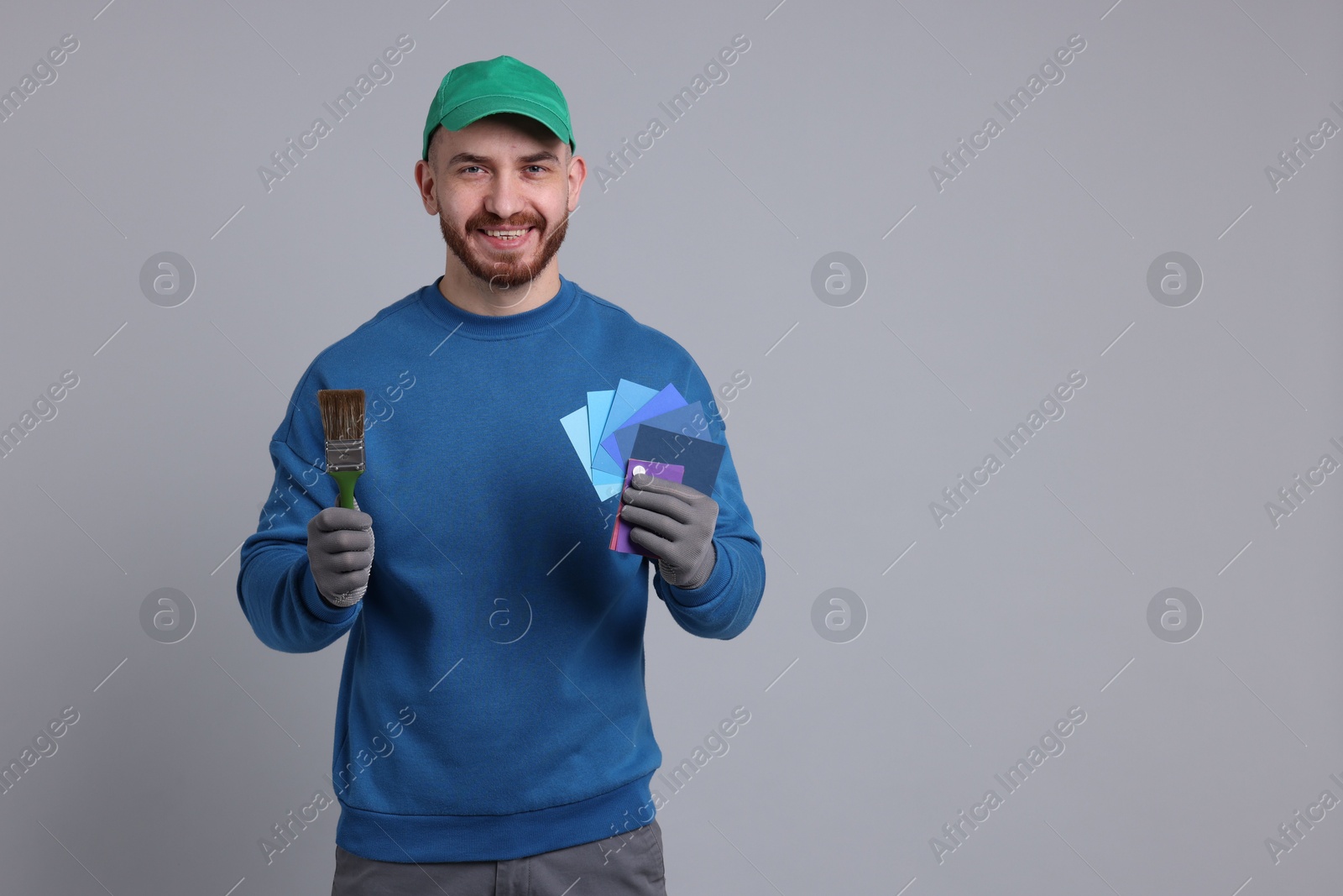 Photo of Man with paintbrush and color samples on light grey background. Space for text